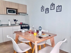 Eine moderne Küche mit Esstisch für zwei Personen, weißen Stühlen, einer Mikrowelle, einem Herd und einem kleinen Topfpflanzen an der Wand.