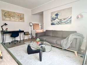 A living room with a grey sofa, a glass coffee table, a desk with a chair, and a large painting on the wall. - 28- Incredible Oriental Style Apt. /Palermo Soho (Buenos Aires)