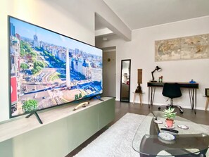 A modern living room with a large flat-screen TV mounted on a wall, a glass coffee table with decorative items, a black office chair, and a desk with a lamp. - 28- Incredible Oriental Style Apt. /Palermo Soho (Buenos Aires)