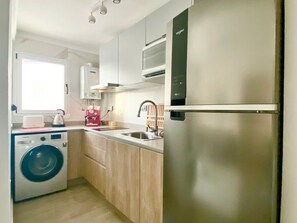 Eine kleine Küche mit Waschmaschine, Spüle und einem Edelstahl-Kühlschrank.