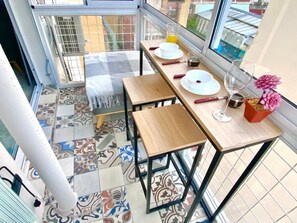 Ein Balkon mit Esstisch für zwei Personen, einem Topfpflanzen und Blick auf die Stadtlandschaft.