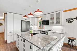 Una cocina moderna con armarios blancos, una isla central y lámparas colgantes rojas.