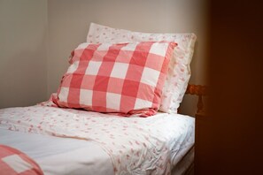 A bed with a checkered pillow and a floral-patterned bedspread. - Stunning Crystal Lake Views | Private Hot Tub | Sleeps 10 | Near Beulah (Beulah)