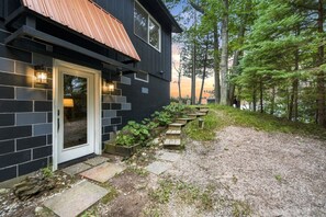 Et moderne hus med mørk facade, en trædør og en grussti, der fører til en træterrasse.