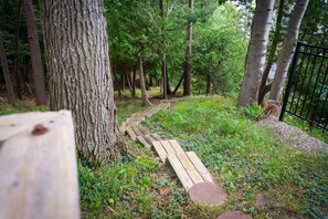 A wooden pathway leading through a wooded area with trees and a metal fence. - Stunning Crystal Lake Views | Private Hot Tub | Sleeps 10 | Near Beulah (Beulah)