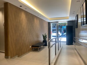 En modern hotellobby med en väggpanel av trä, en bänk, en krukväxt och en glasdörr som leder ut.