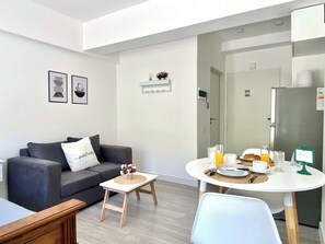 A modern living room with a sofa, a small table with breakfast items, and a dining area with a chair. - 201- Modern Apt. w/ Great Amenities in Palermo (Buenos Aires)
