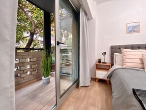 A bedroom with a bed, bedside table, lamp, and a view through a sliding glass door to an outdoor area with a potted plant. - 24- Modern Space in Palermo w/ Pool 2 Beds. (Buenos Aires)