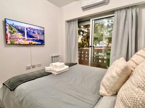 A hotel room with a bed, a TV mounted on the wall, a window with curtains, and a view of the outdoors. - 24- Modern Space in Palermo w/ Pool 2 Beds. (Buenos Aires)