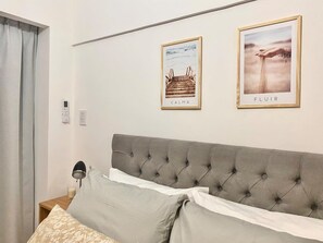 Ein Schlafzimmer mit einer gepolsterten Kopfteil, einem Nachttisch mit Lampe und zwei gerahmten Bildern an der Wand.