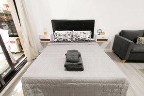 A hotel room with a bed, a grey sofa, and a nightstand with a lamp. - 30- Modern Apt. w/ Great Amenities in Palermo (Buenos Aires)