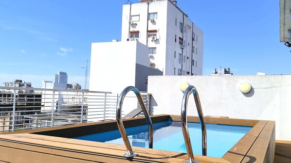 Une piscine sur le toit, accessible par deux échelles en métal, et entourée d’une terrasse en bois.