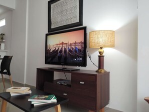 A television on a wooden stand with a lamp beside it, a table with books, and a framed picture on the wall. - 29- Unbeatable Apt w/Amenities on Terrace - Palermo (Buenos Aires)