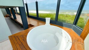 A modern bathroom with a large bathtub, wooden flooring, and a view of the ocean through large windows.