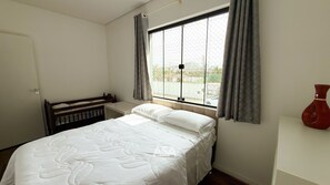 Quarto com cama, janela com cortinas, mesa de cabeceira e um vaso na parede.