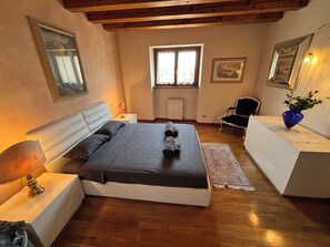Un dormitorio con cama, mesitas de noche, una silla, un ventanal y un radiador.