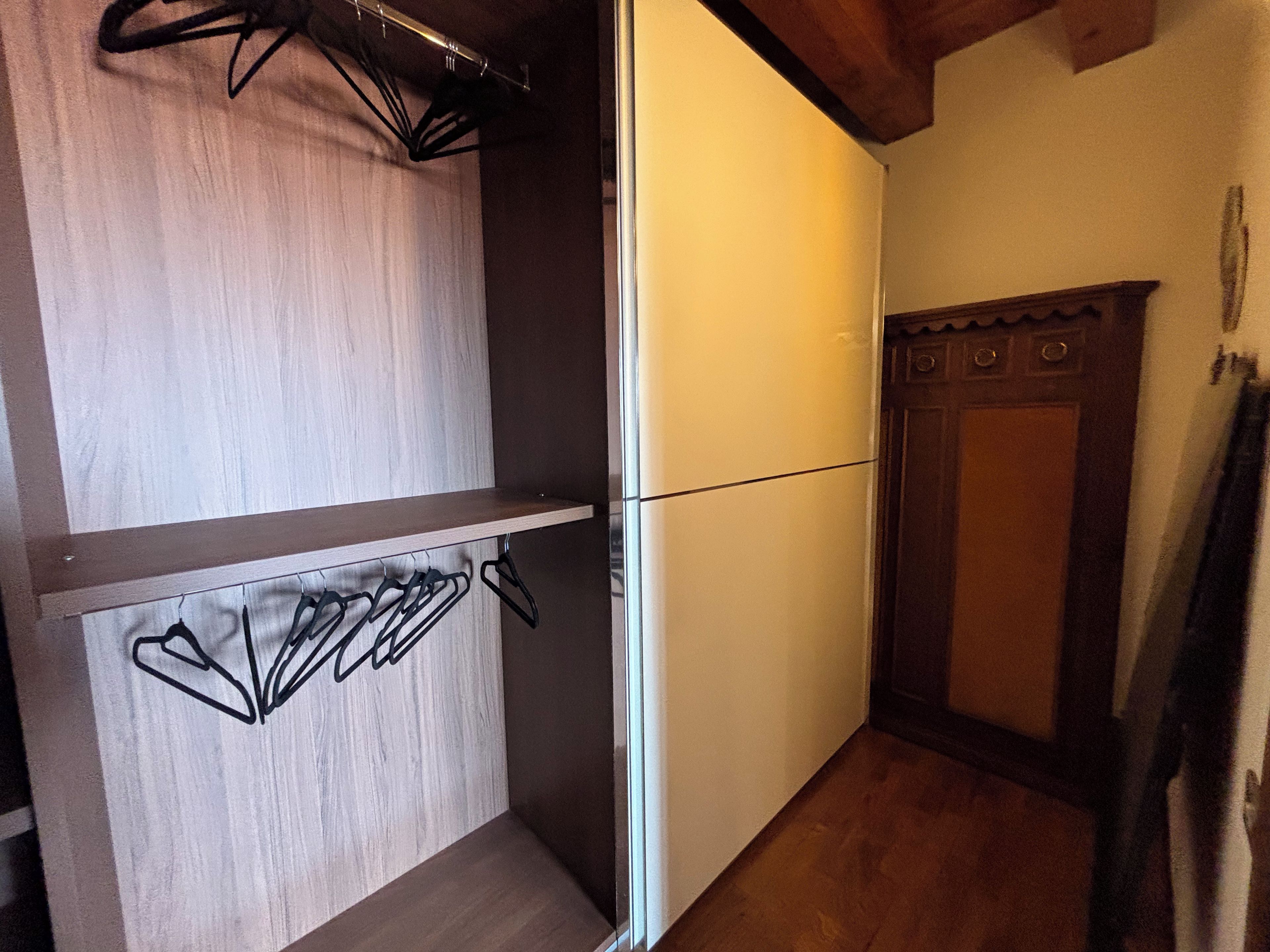 A compact kitchen with a built-in refrigerator, wooden cabinets, and a hanging clothes rack.
