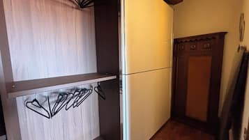 A compact kitchen with a built-in refrigerator, wooden cabinets, and a hanging clothes rack.