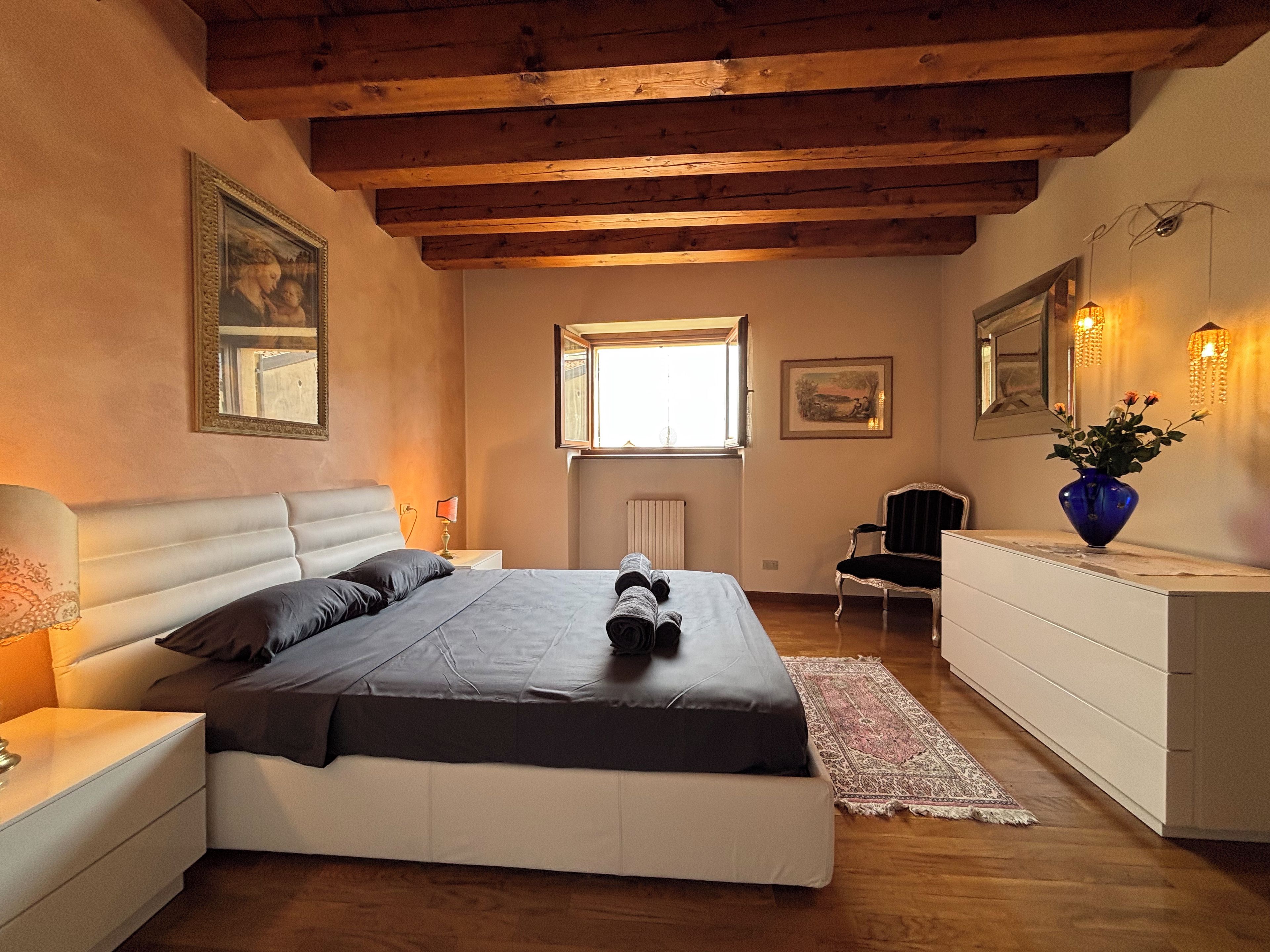 A bedroom with a bed, bedside tables, a dresser, a chair, a window, and wall-mounted lights.