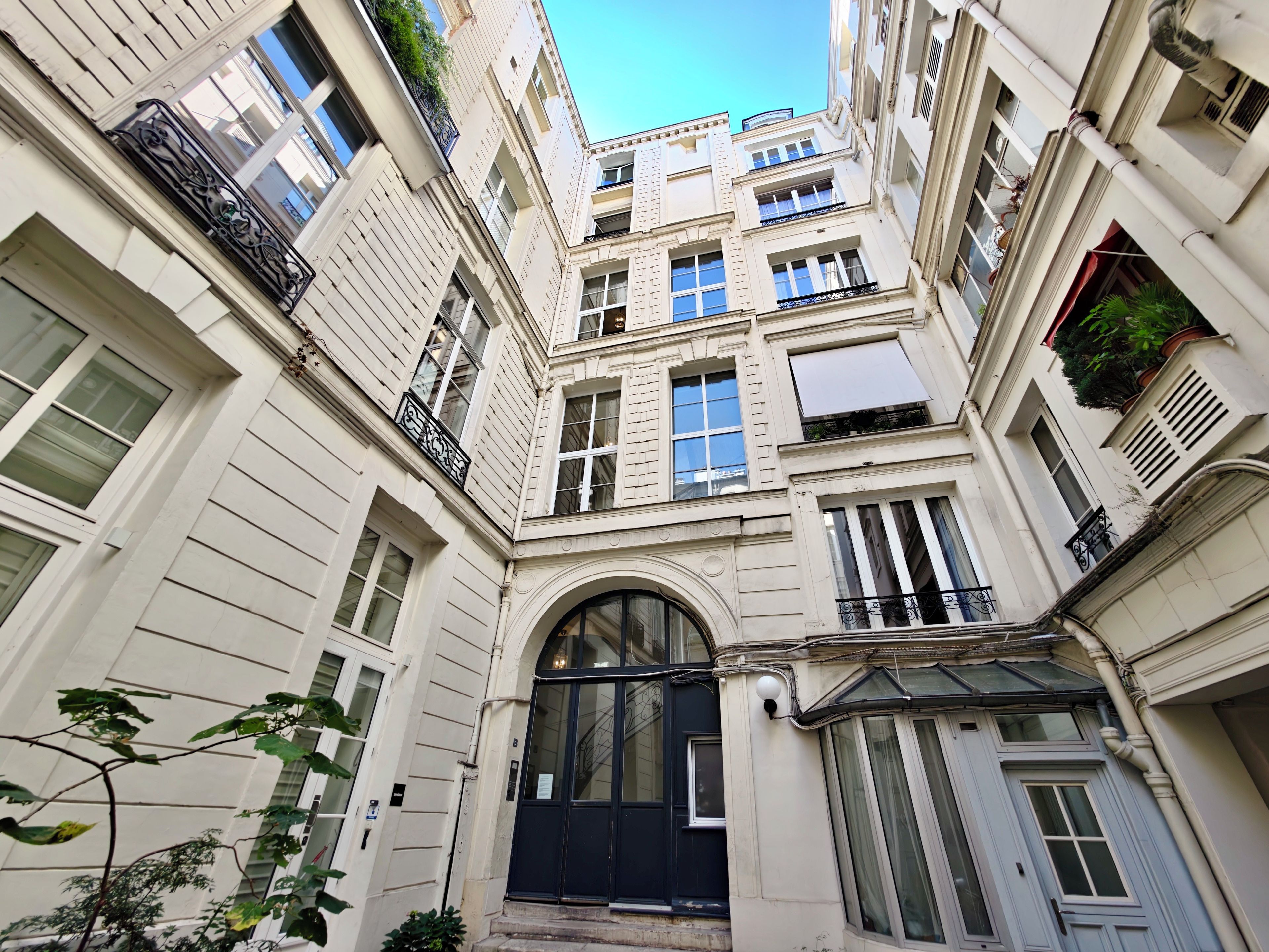 Un immeuble à plusieurs étages doté d’une entrée centrale, de grandes fenêtres et de balcons avec des garde-corps.