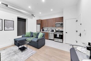 Ein modernes Apartment mit grauem Sofa, Küchenbereich und Esstisch für zwei Personen.
