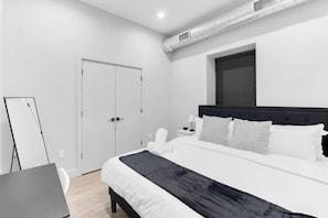 A modern hotel room with a bed, bedside table, and a desk with a chair. - Serene 1-BR KING Sanctuary– 20 Minutes to NYC! (Newark)