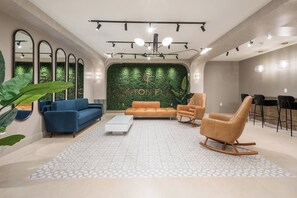 Una sala moderna con una pared verde, sofás azules y naranjas, una mesa de centro blanca y una zona de estar con bar.