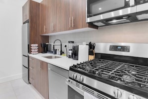 A modern kitchen with a stainless steel stove, wooden cabinets, a built-in microwave, and a sink. - Serene 1-BR KING Sanctuary– 20 Minutes to NYC! (Newark)