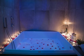 Uma banheira com pétalas de rosas flutuando na água, cercada por velas e uma garrafa de champanhe.
