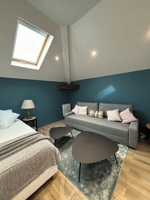 Ein modernes Schlafzimmer mit Bett, einer Couch, einem kleinen Tisch und einem Oberlicht.