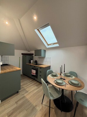 A modern kitchen with a skylight, a dining area with a round table, and a small island with a built-in oven. - New Listing (Choisy-le-Roi)