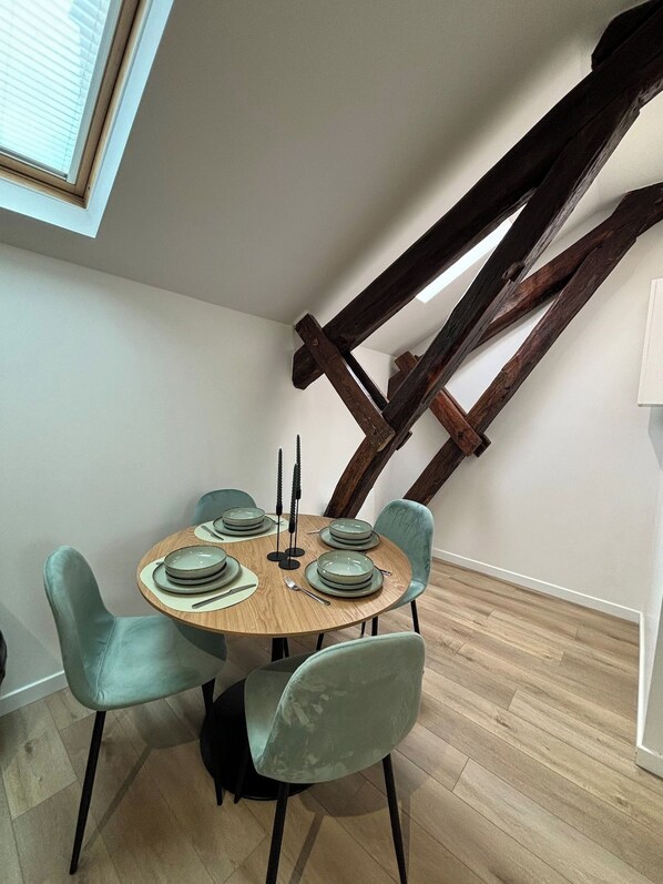 Ein Essbereich mit einem runden Holztisch, gedeckt für vier Personen, umgeben von vier stählfarbenen Stühlen.