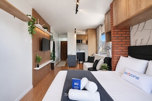 A modern hotel room with a bed, a desk, a kitchenette, and a view of the outside. - Studio in Condo. 700m From Beach Bou0203 (Florianópolis)
