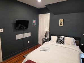 A bedroom with a bed, a television mounted on the wall, a door, and a small table with a lamp. - Enjoyable 4-bedroom house with AC in charming Meriden (Meriden)