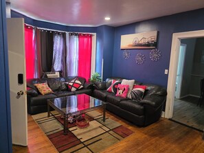 A living room with a sectional sofa, a glass coffee table, and a patterned rug. - Enjoyable 4-bedroom house with AC in charming Meriden (Meriden)