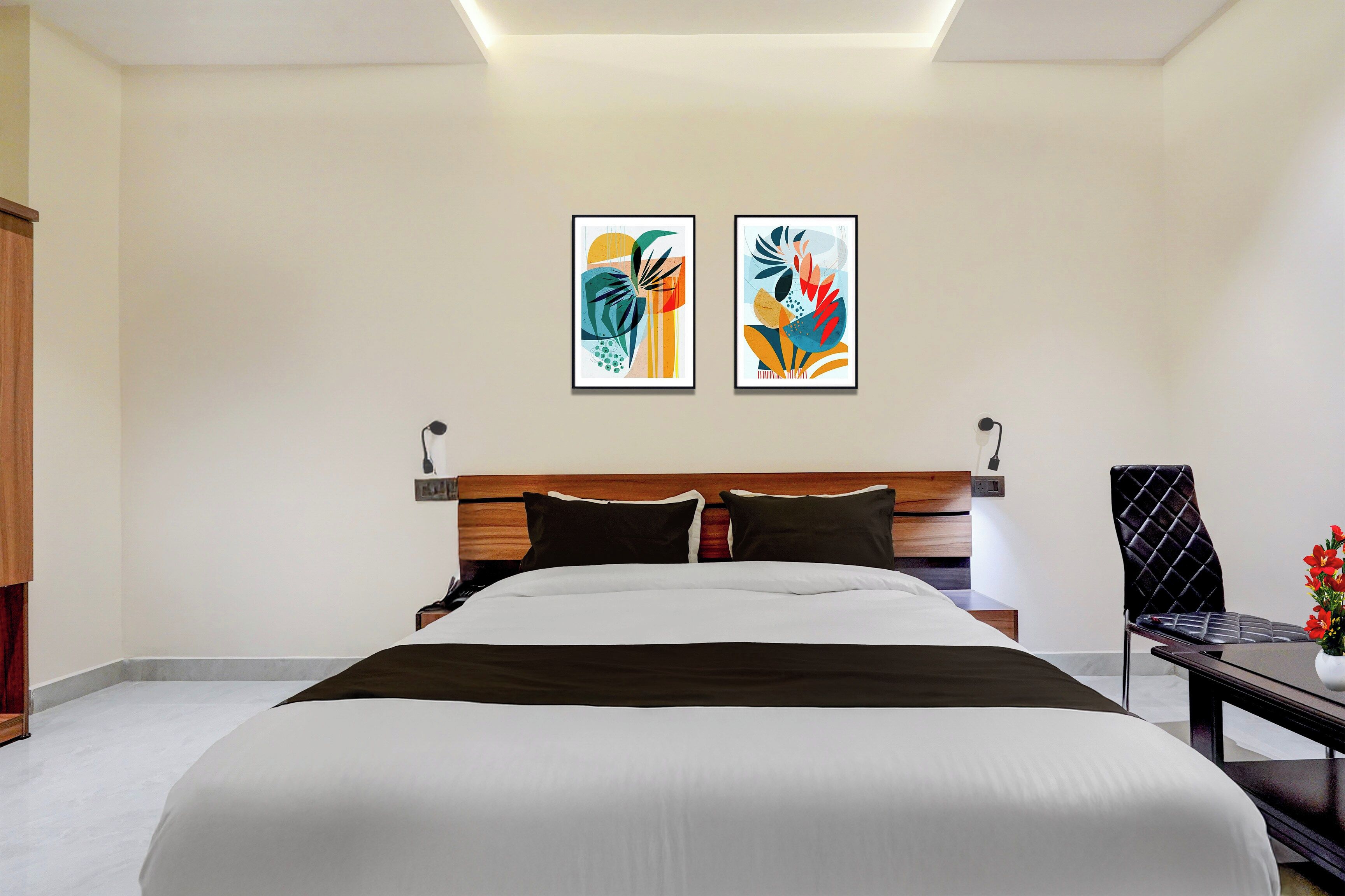 A hotel room with a bed, a desk, and two framed artworks on the wall.