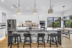 A modern kitchen with a marble island, stainless steel appliances, and a large window offering a view of the outdoors. - Sarasota Coastal Retreat (Sarasota)