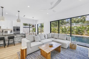 A modern living room with a sectional sofa, a wooden coffee table, and a view of a swimming pool. - Sarasota Coastal Retreat (Sarasota)