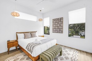 A bedroom with a bed, bedside tables, a bench, a hanging light, and large windows. - Sarasota Coastal Retreat (Sarasota)