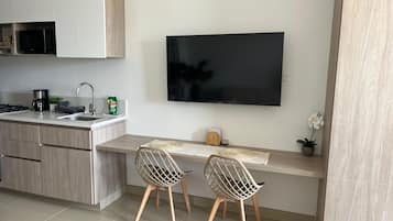 Una cocina moderna con televisor de pantalla plana, dos sillas, cafetera y microondas.