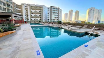 Una piscina al terrat amb gandules, envoltada d'edificis residencials alts.