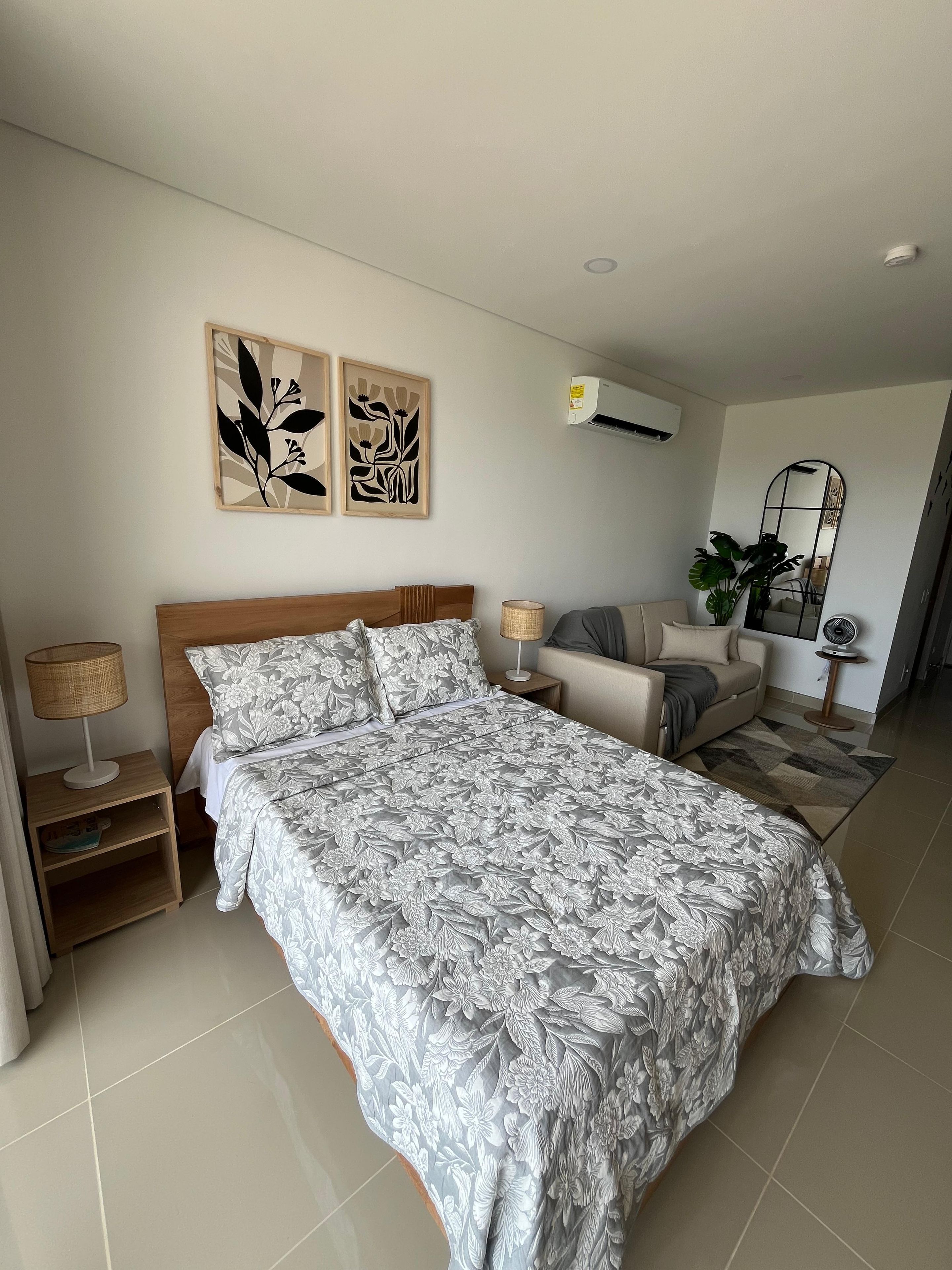 Ein Schlafzimmer mit einem großen Bett, einem Nachttisch mit Lampe, einer Couch, einem Spiegel und Wandbildern.