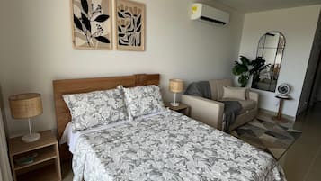 A bedroom with a large bed, a bedside table with a lamp, a sofa, a mirror, and wall art.