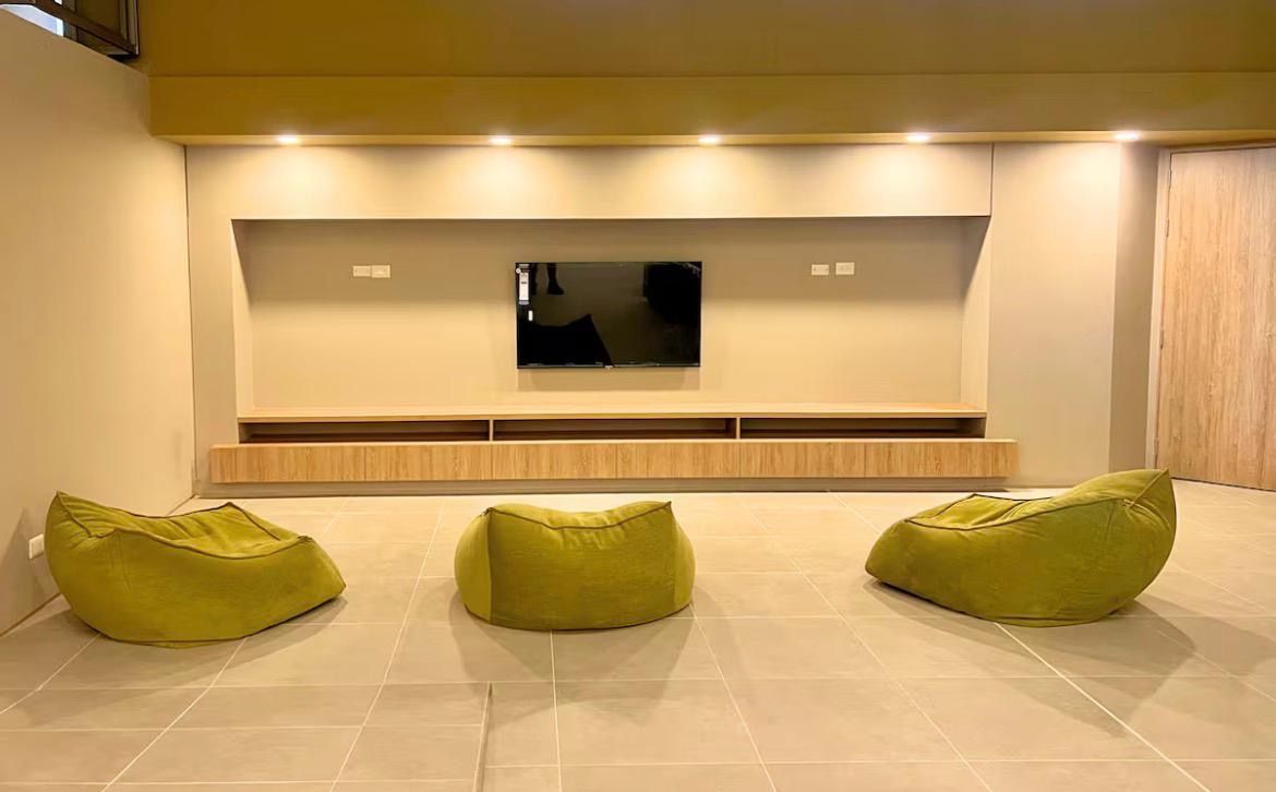 Una sala de estar moderna con un televisor de pantalla plana montado en la pared, un mueble de madera debajo y tres sillones informales color verde.