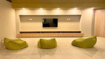 Una sala de estar moderna con un televisor de pantalla plana montado en la pared, un mueble de madera debajo y tres sillones informales color verde.