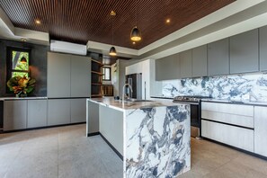 A modern kitchen with a marble island, grey cabinetry, and a wooden ceiling. - Casa Horizonte Azul. Where the jungle ends and the blue begins in Dominical CR (Savegre de Aguirre)