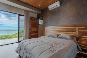 A bedroom with a large bed, wooden headboard, and a view of the sea through a sliding door. - Casa Horizonte Azul. Where the jungle ends and the blue begins in Dominical CR (Savegre de Aguirre)