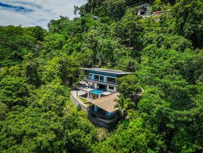 A modern house surrounded by dense forest, with a swimming pool and a thatched-roof structure nearby. - Casa Horizonte Azul. Where the jungle ends and the blue begins in Dominical CR (Savegre de Aguirre)