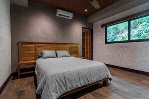 Un dormitorio con una cama de madera, una ventana con vistas a zonas verdes y un equipo de aire acondicionado en la pared.
