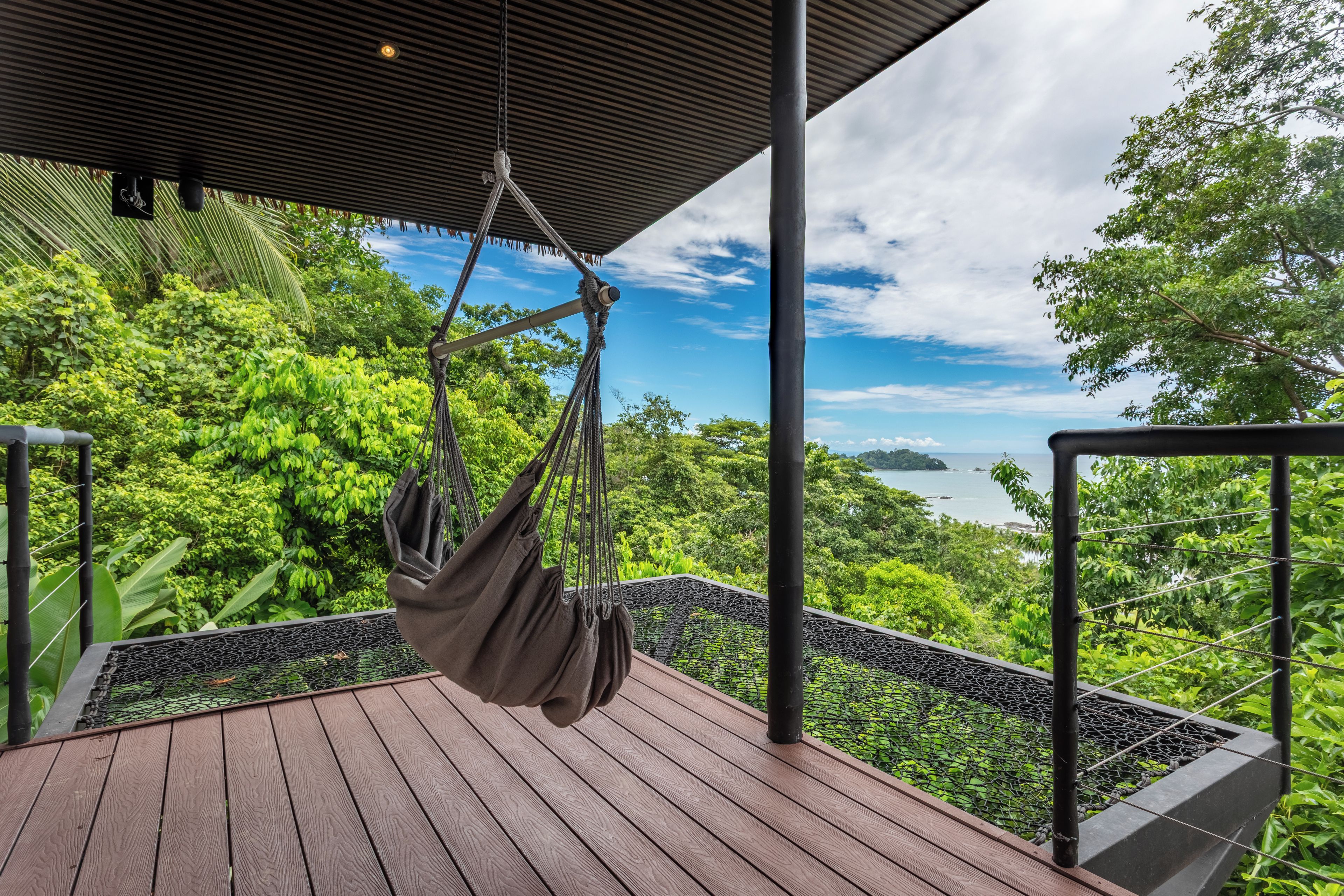A hammock suspended from a ceiling, overlooking a lush green landscape with a body of water in the distance.